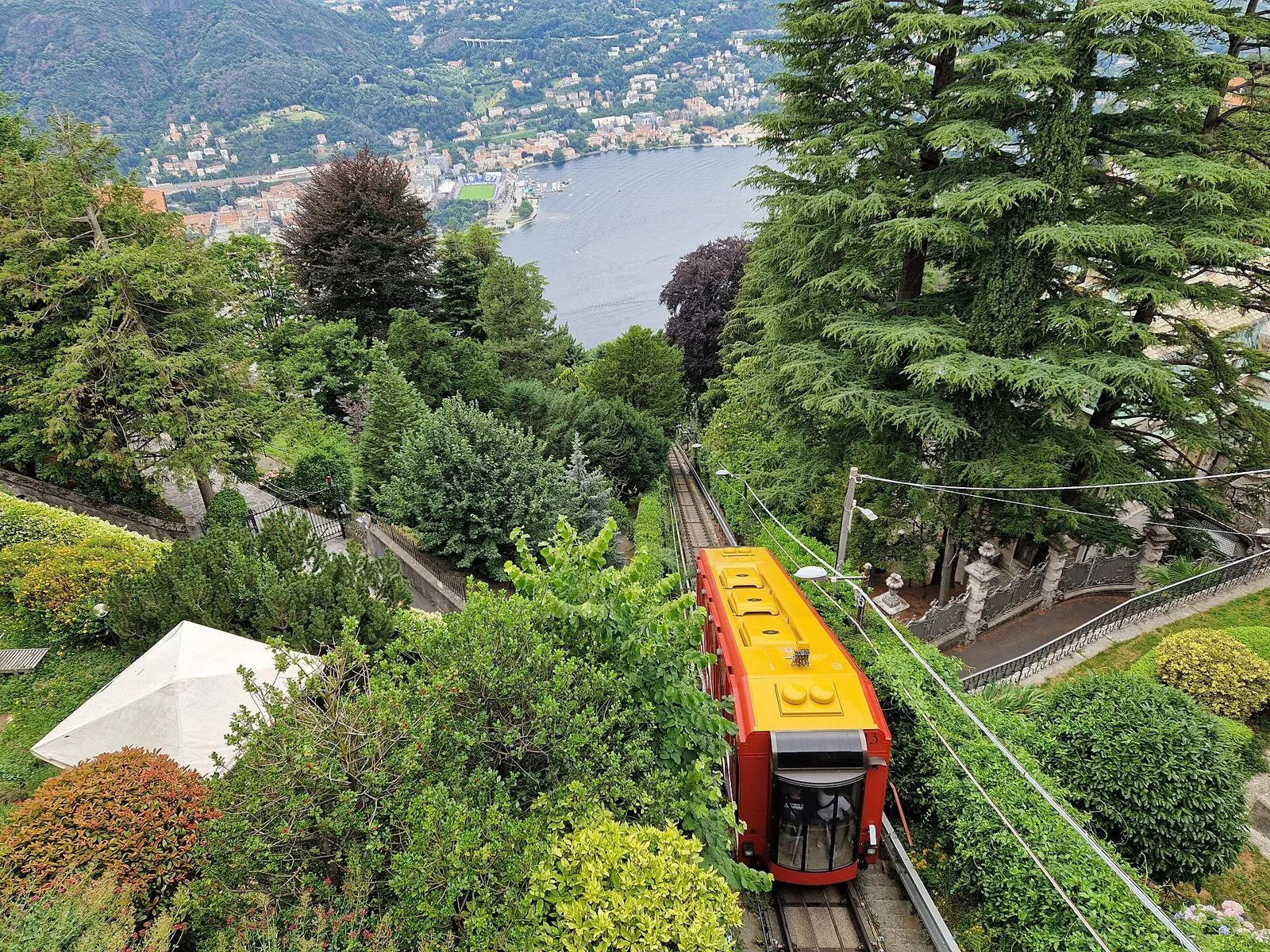 Vettura rossa e gialla della funicolare Como-Brunate tra il verde, con Como e il lago sullo sfondo