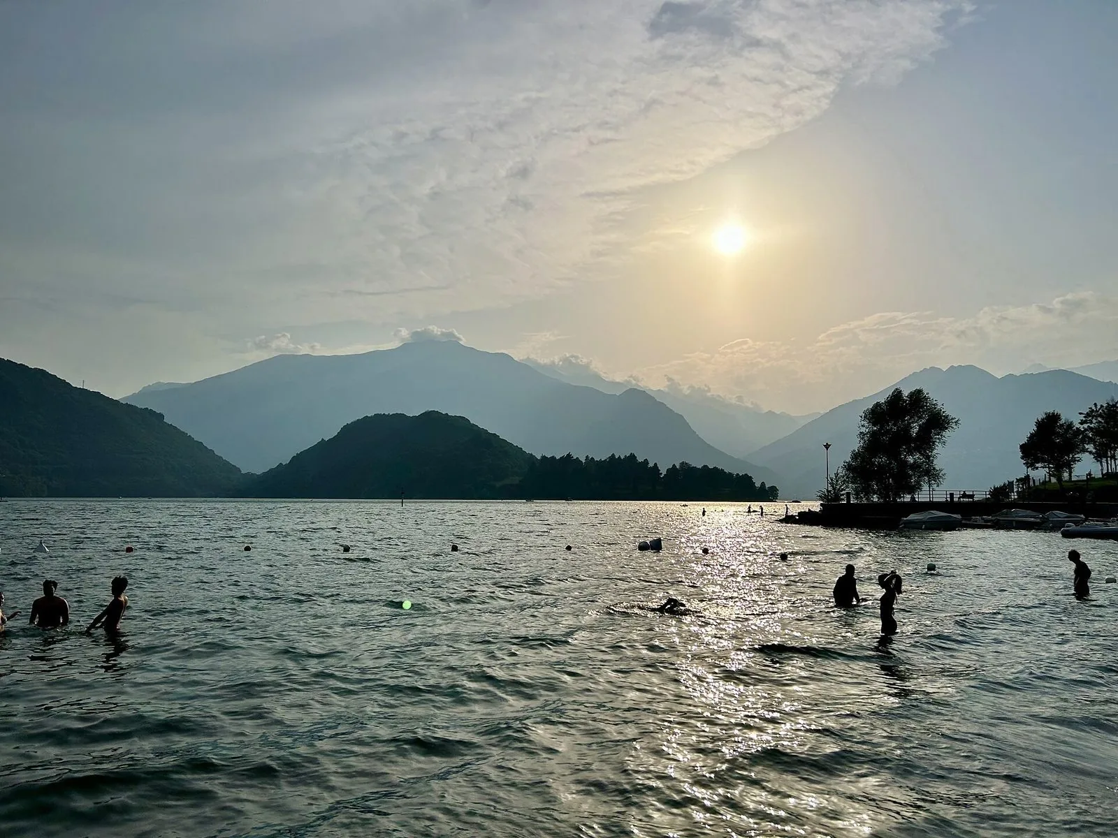 Bagnanti nel Lago di Como al tramonto d'estate con le montagne sullo sfondo