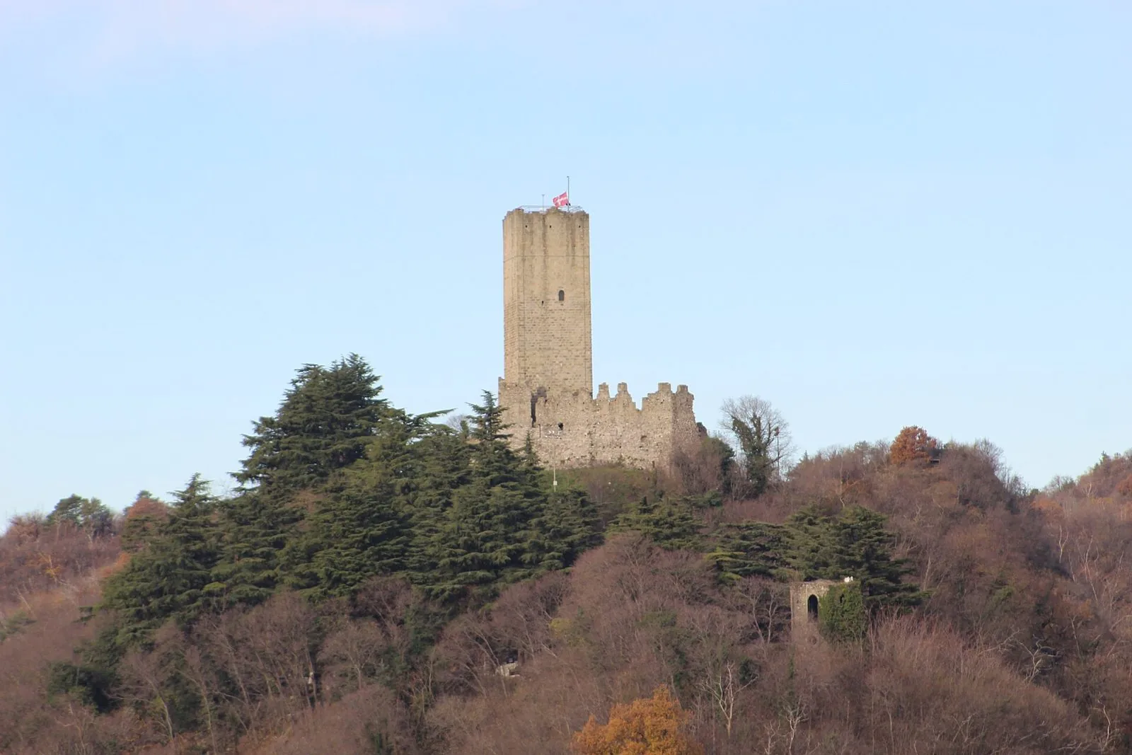 La torre del Castello Baradello con la bandiera di Como sopra le colline boscose del Parco Spina Verde